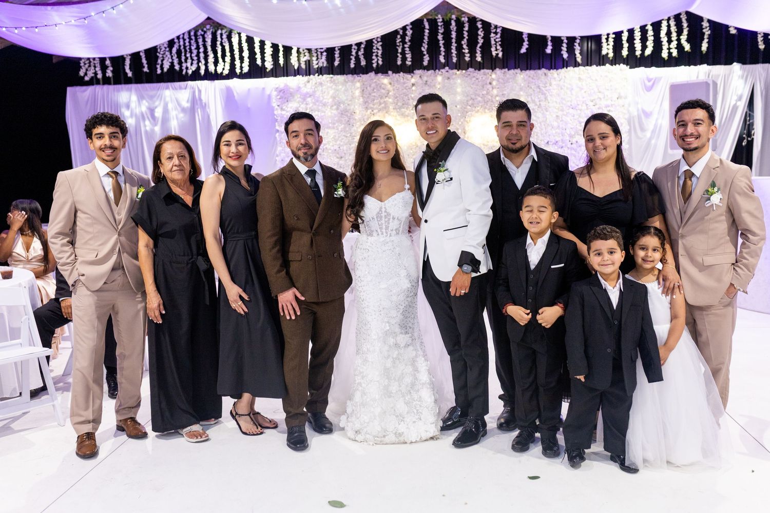 Wedding party and guests posing for group photos against a white backdrop with purple lighting.