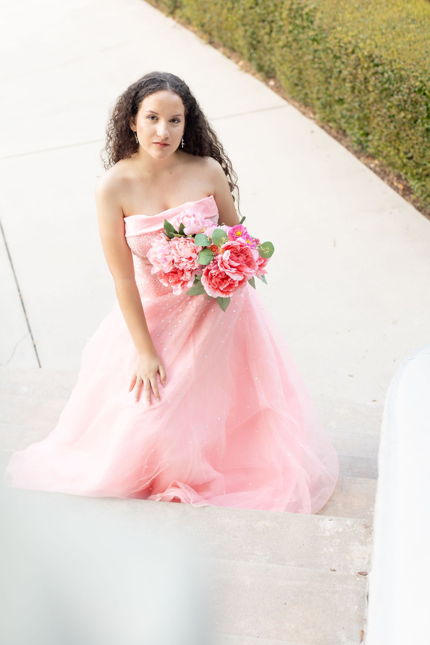 Model in flowing pink tulle gown with floral details poses gracefully outdoors.