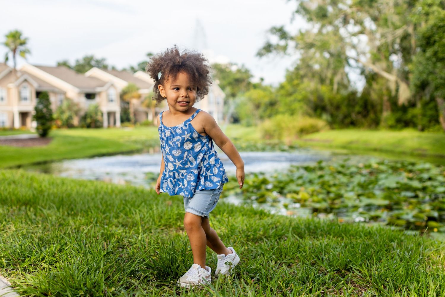 Child plays on grassy hill during summer photo session.