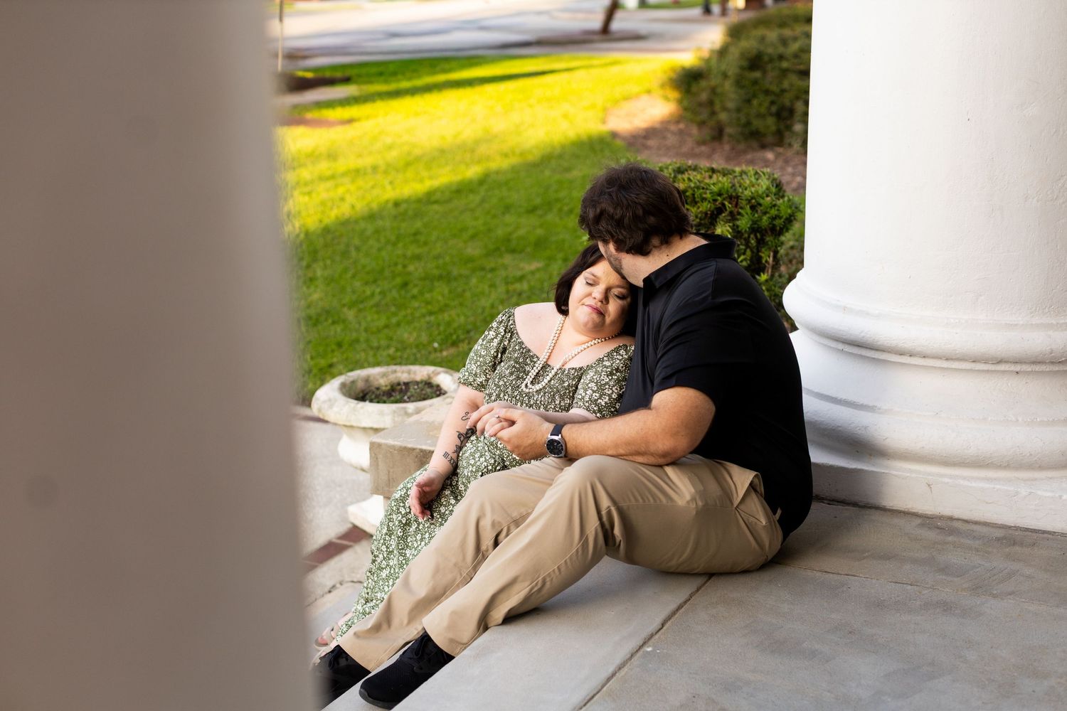 A couple sits together on steps near white columns of a building.