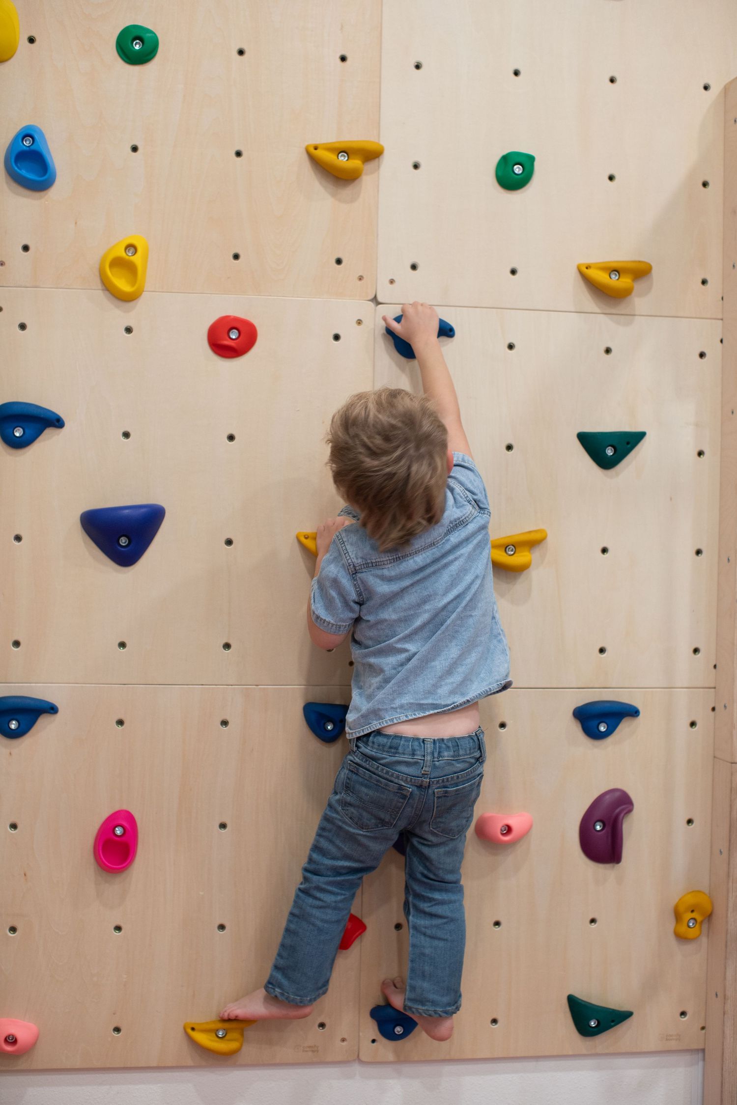 Young child climbs on indoor rock climbing wall with colorful holds.