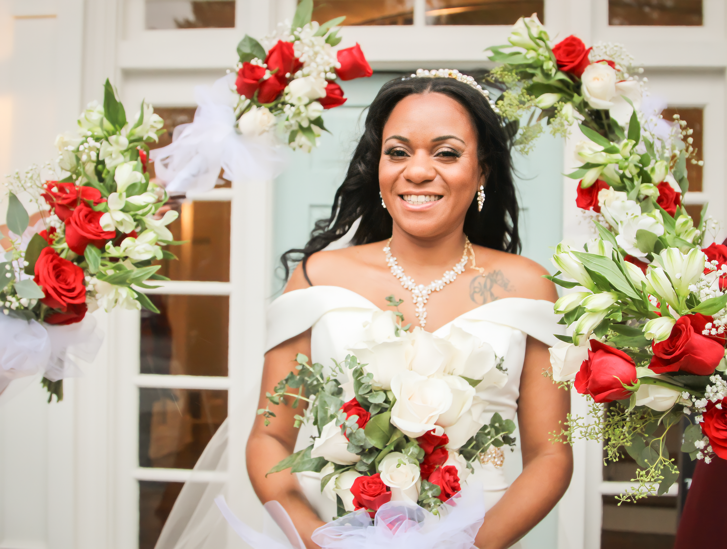 Bride holds stunning red and white rose bouquet in elegant off-shoulder wedding dress.