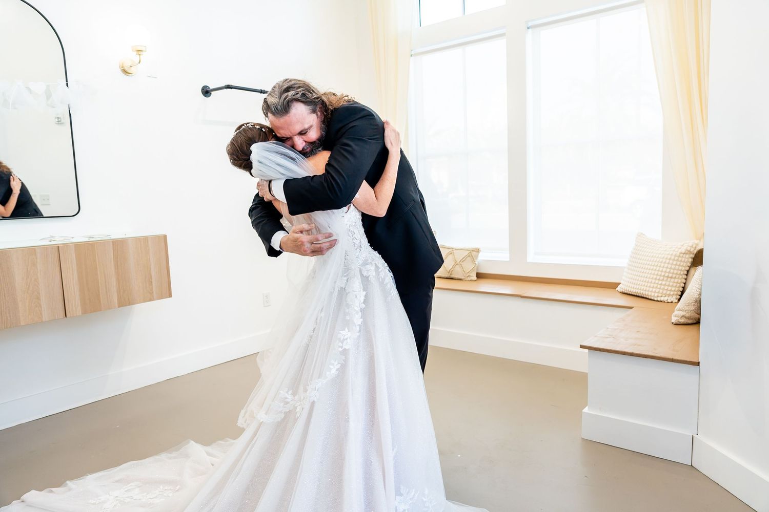 Bride and groom share an emotional first look hug in a bright white bridal suite on their wedding day.