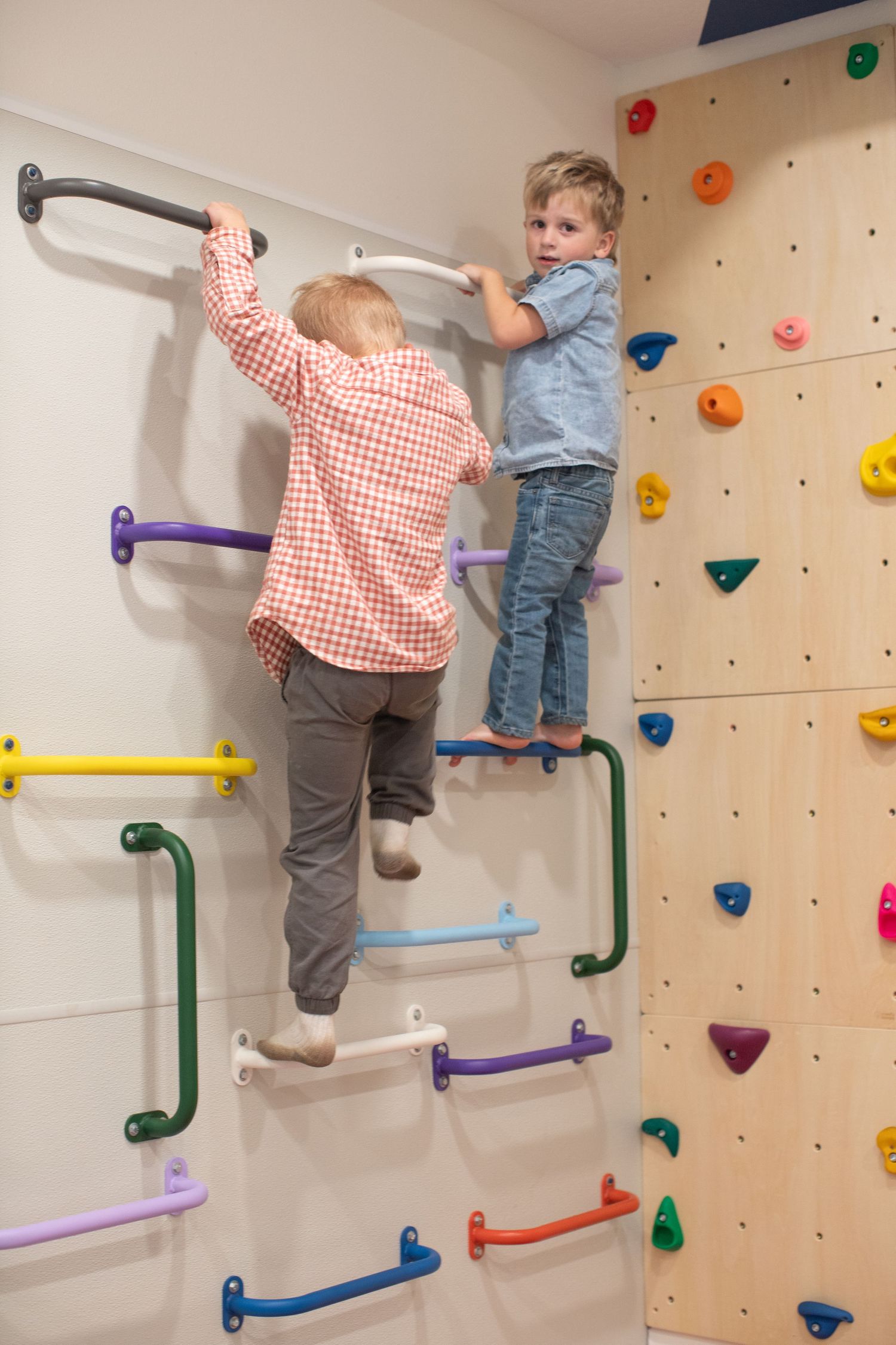 Children climb on indoor wall with colorful handholds and grips.