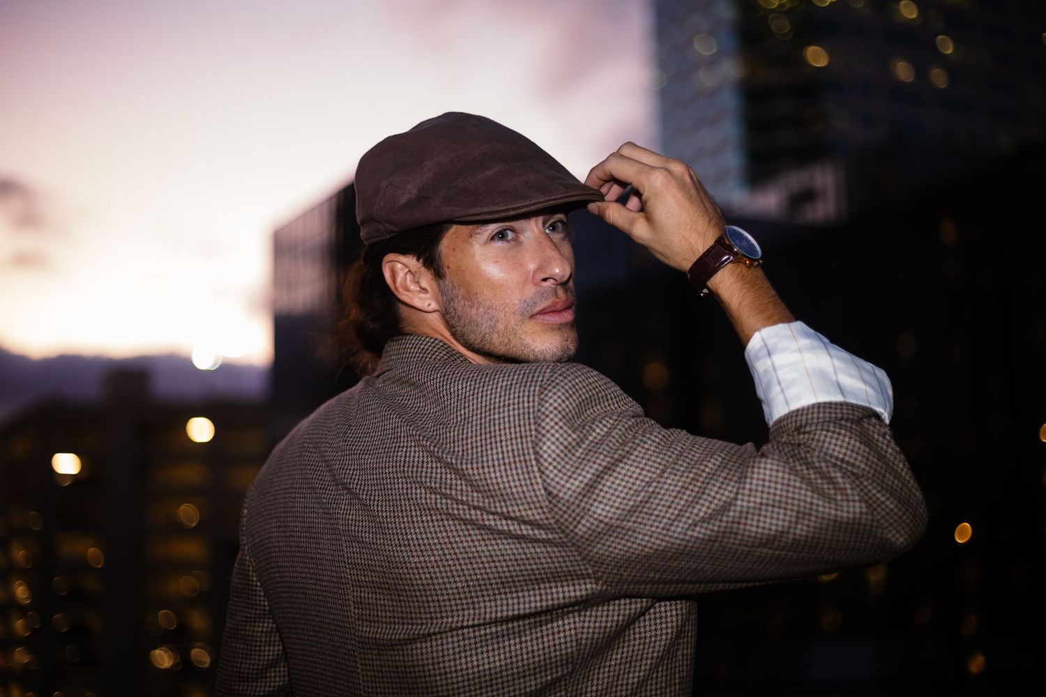 Silhouette of person in hat against city skyline at dusk.