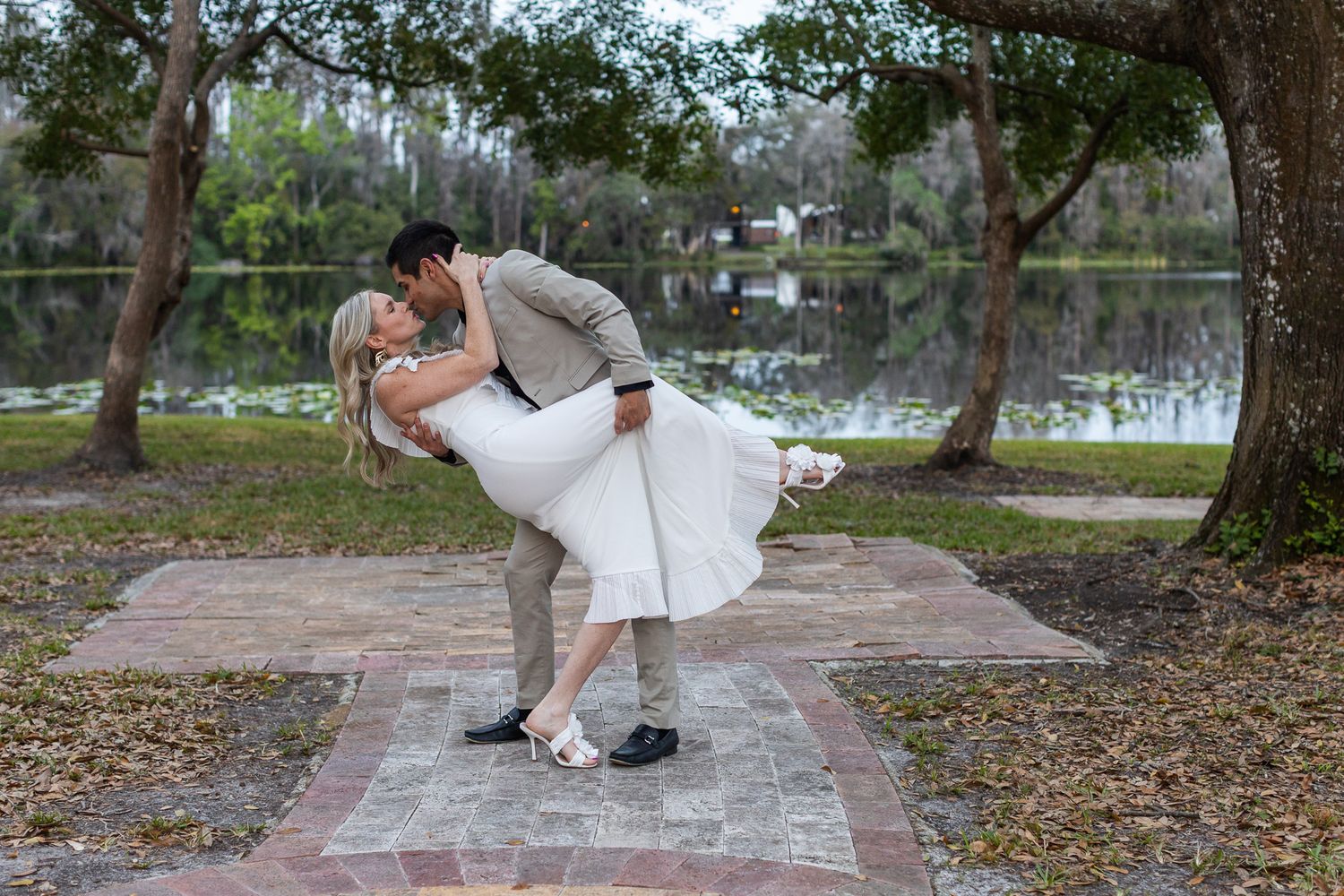 Couple in formal wear performs romantic dip pose in outdoor garden setting.