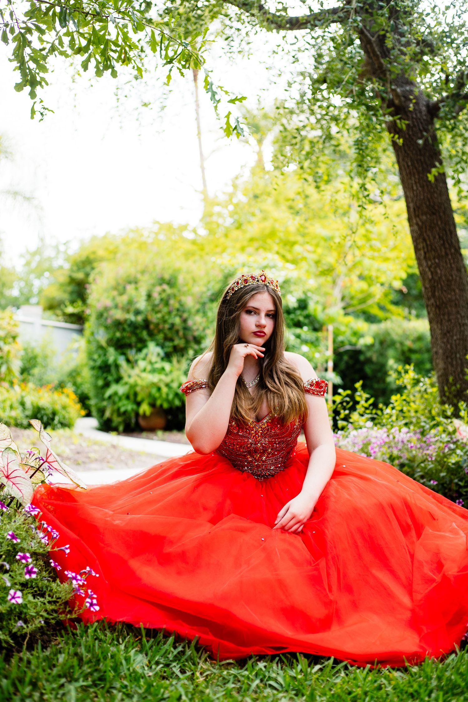 Flowing red formal dress photographed in lush garden setting with natural lighting.