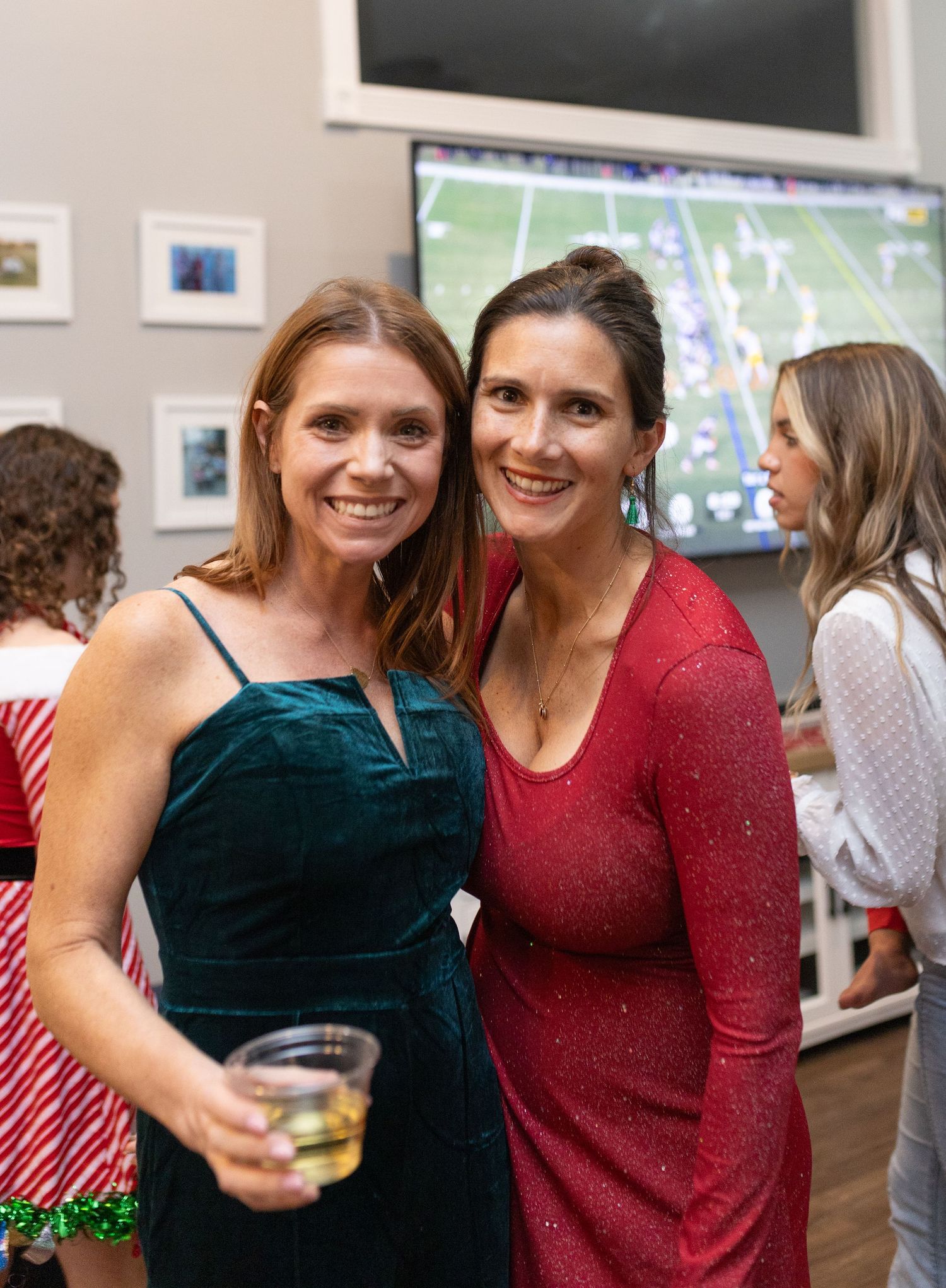 Two guests in festive attire enjoying drinks and conversation at a holiday party.