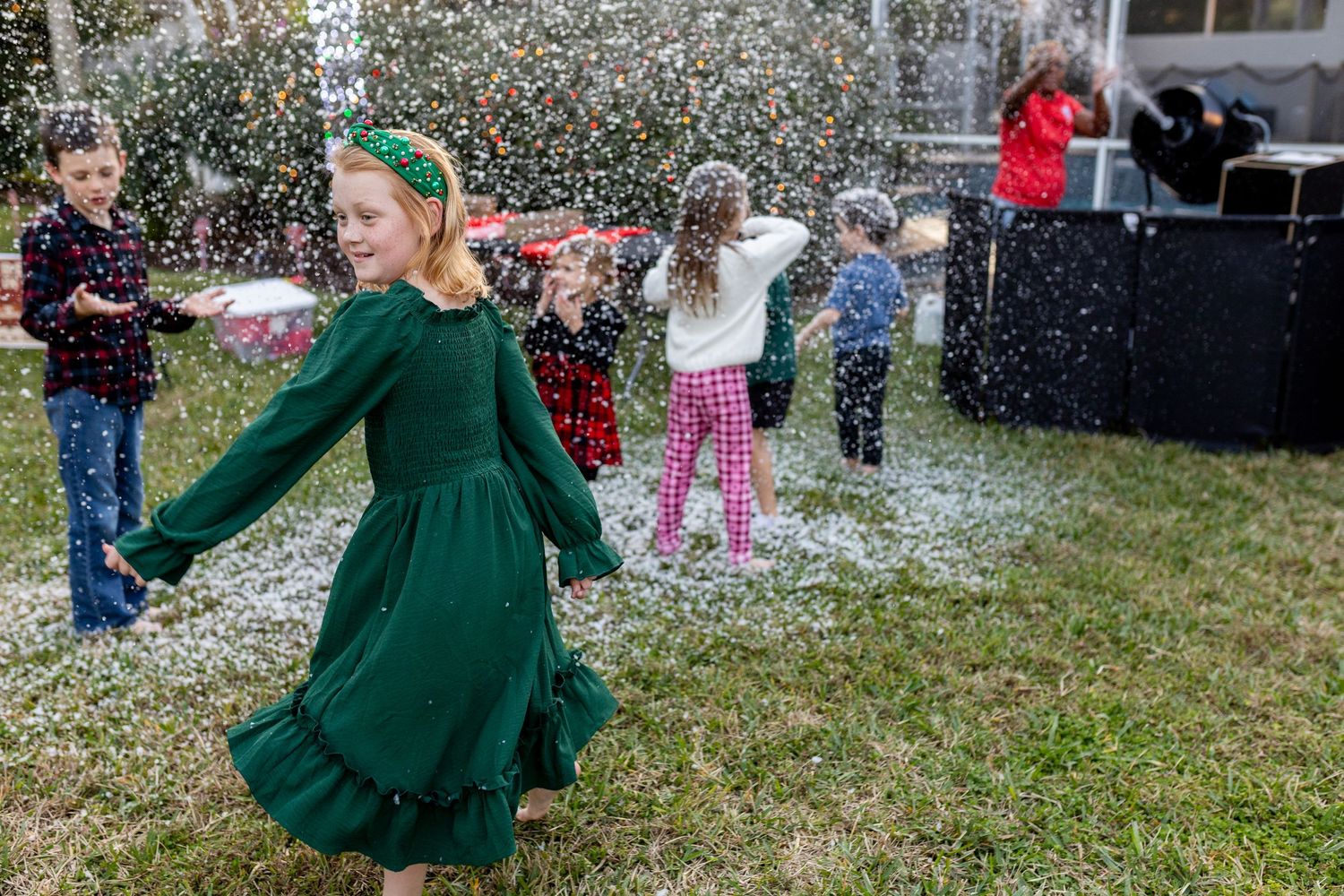 Children and adults enjoying artificial snow at a holiday event.