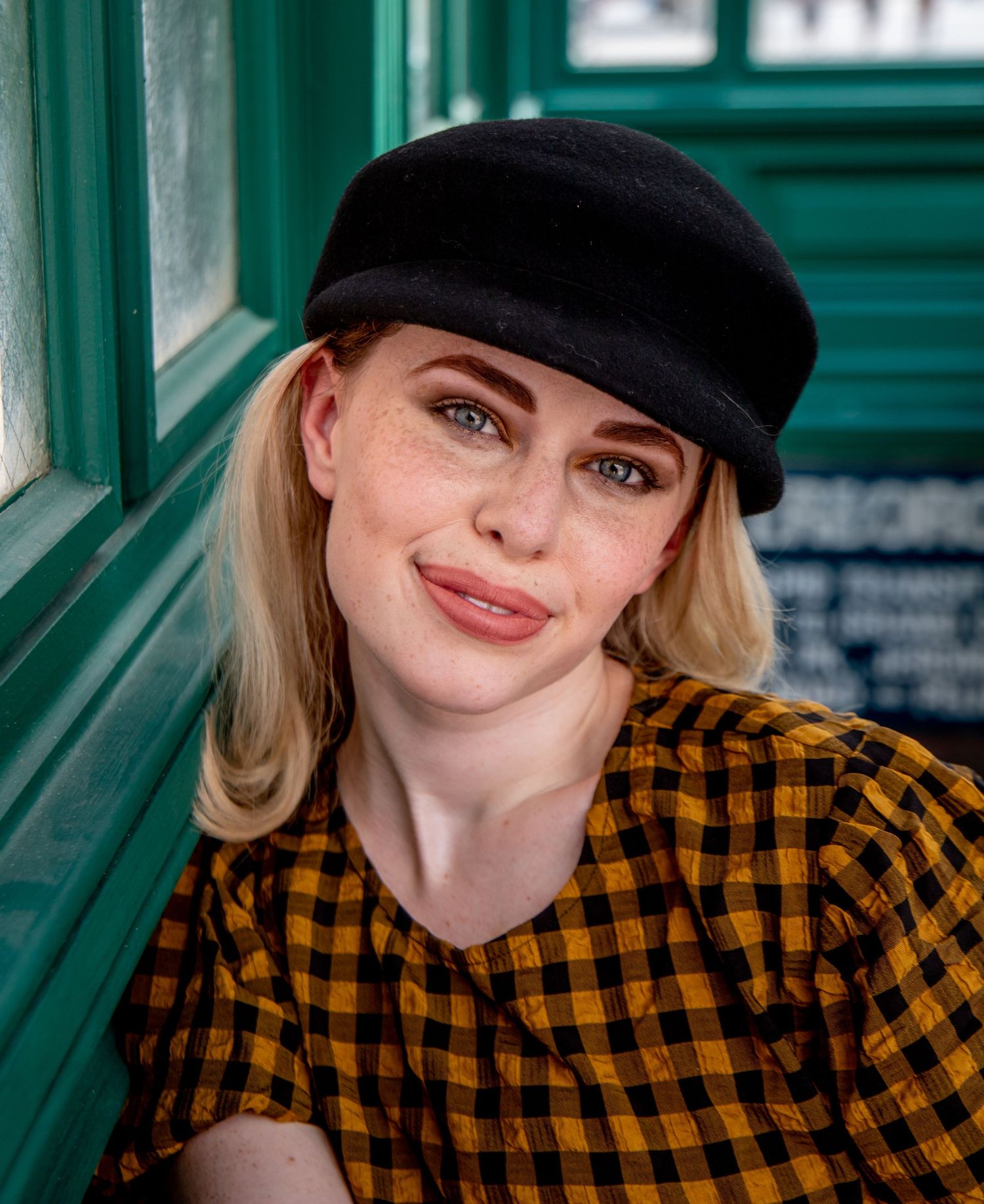 Fashion shoot against green background featuring yellow plaid shirt and black cap.