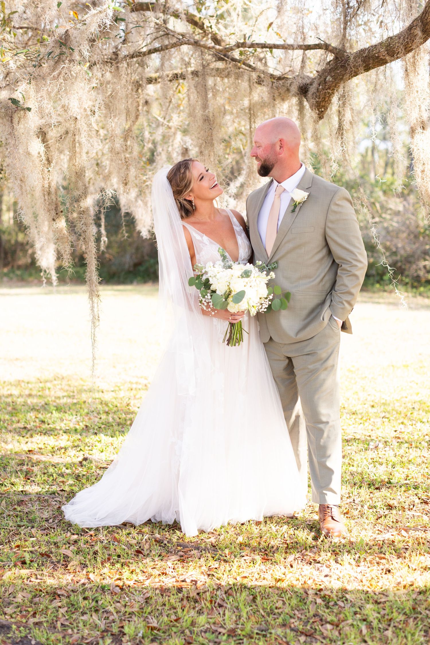 Wedding couple shares romantic moment under Spanish moss draped trees in golden afternoon light.