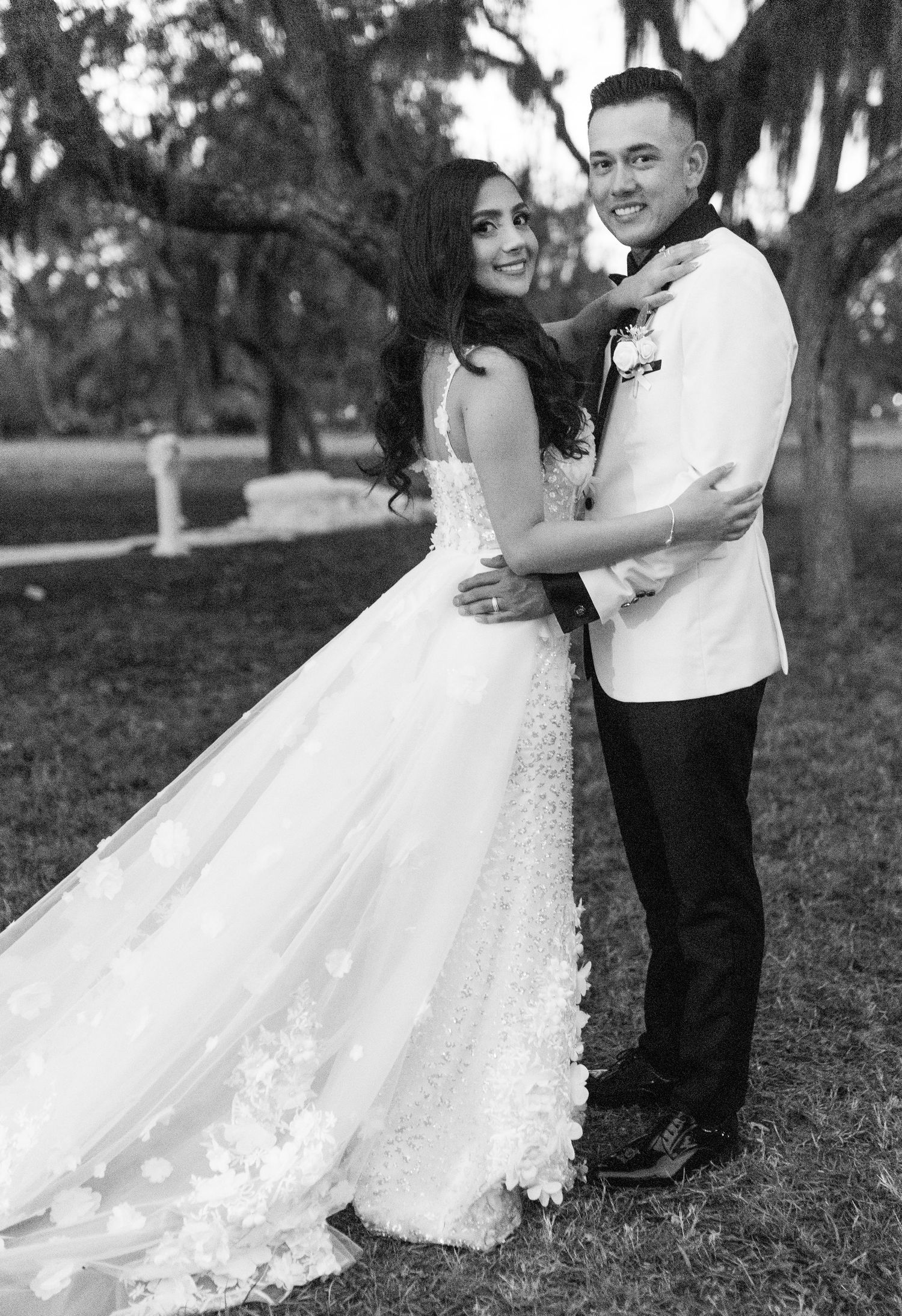 A black and white portrait of a couple in wedding attire embracing outdoors.