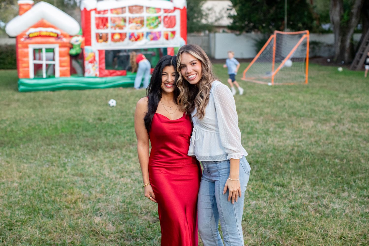 Friends pose together outdoors with red dress and casual attire against carnival backdrop.