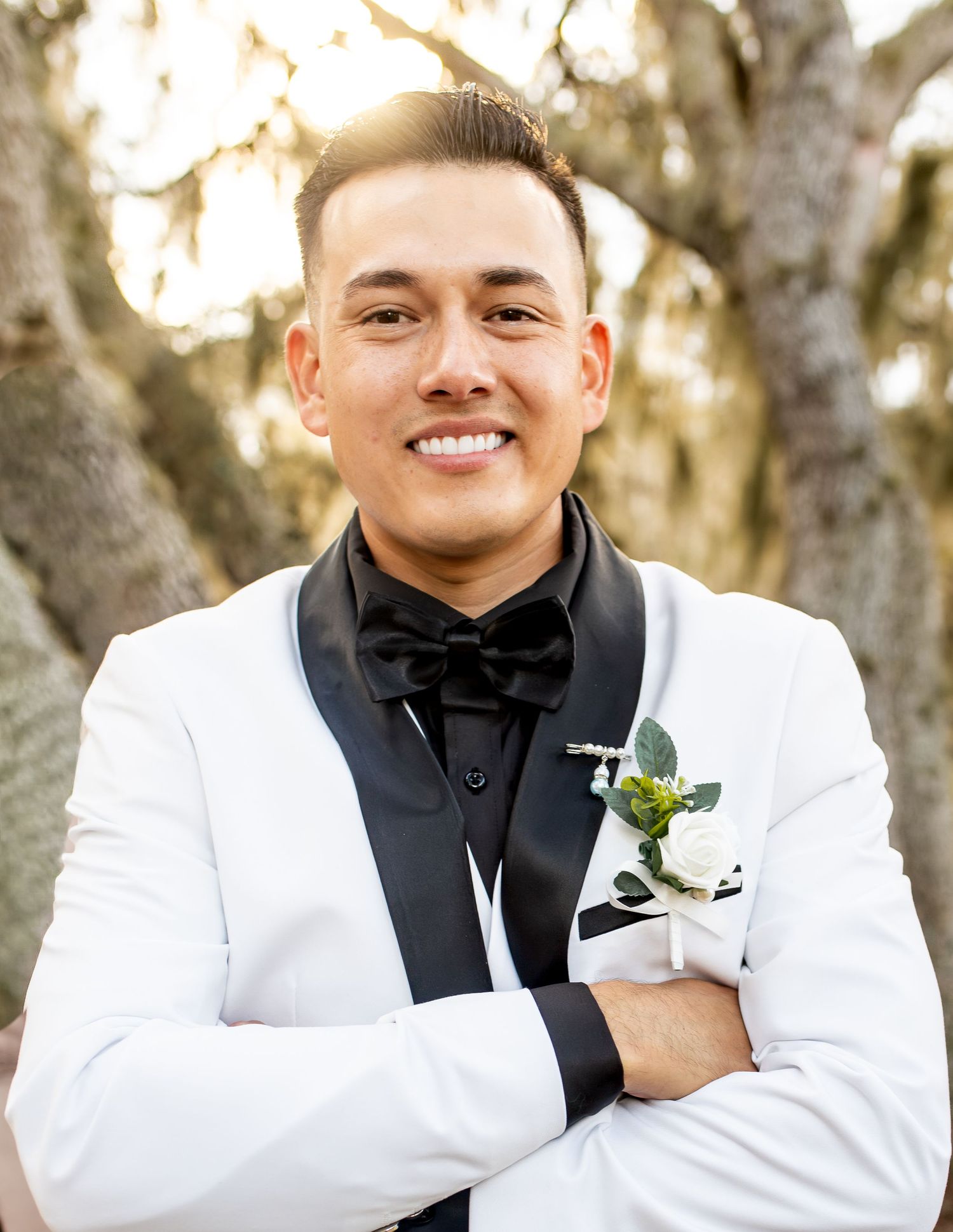 A groom in a white tuxedo jacket and black bow tie poses for formal portraits.