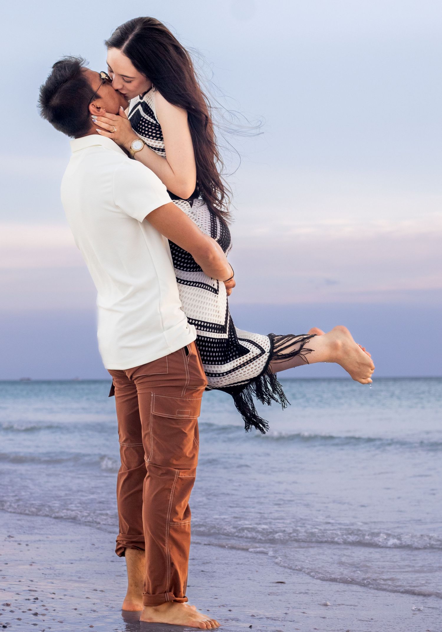 Couple lifting and spinning in joyful dance on beach at sunset.