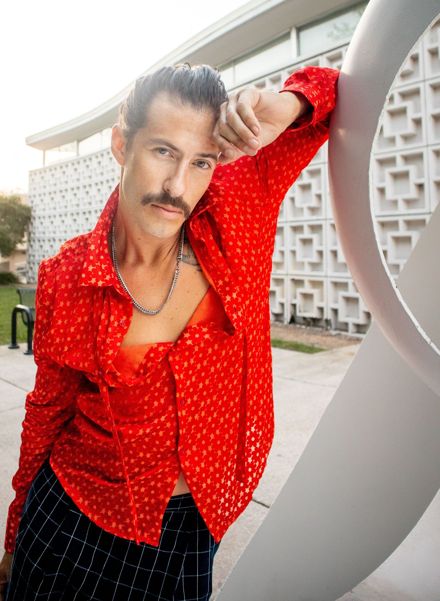 Stylish pose against white architectural wall wearing bright red patterned shirt.