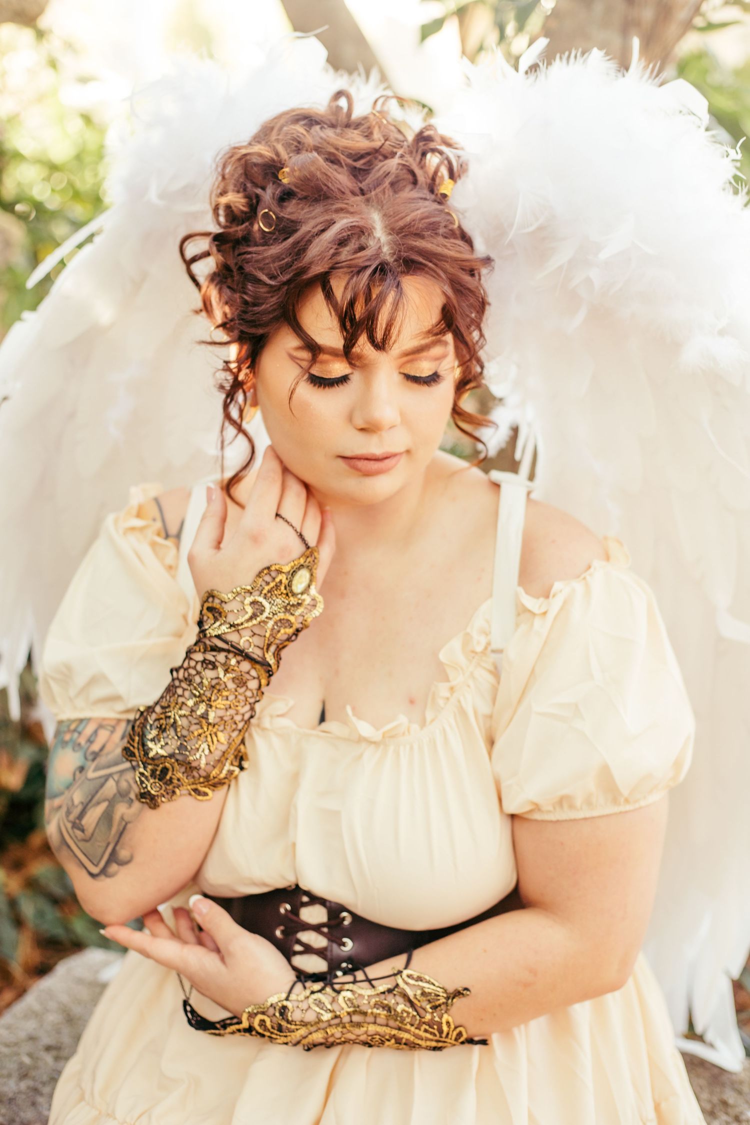 Artistic portrait with angel wings and Victorian-style cream dress in natural lighting.