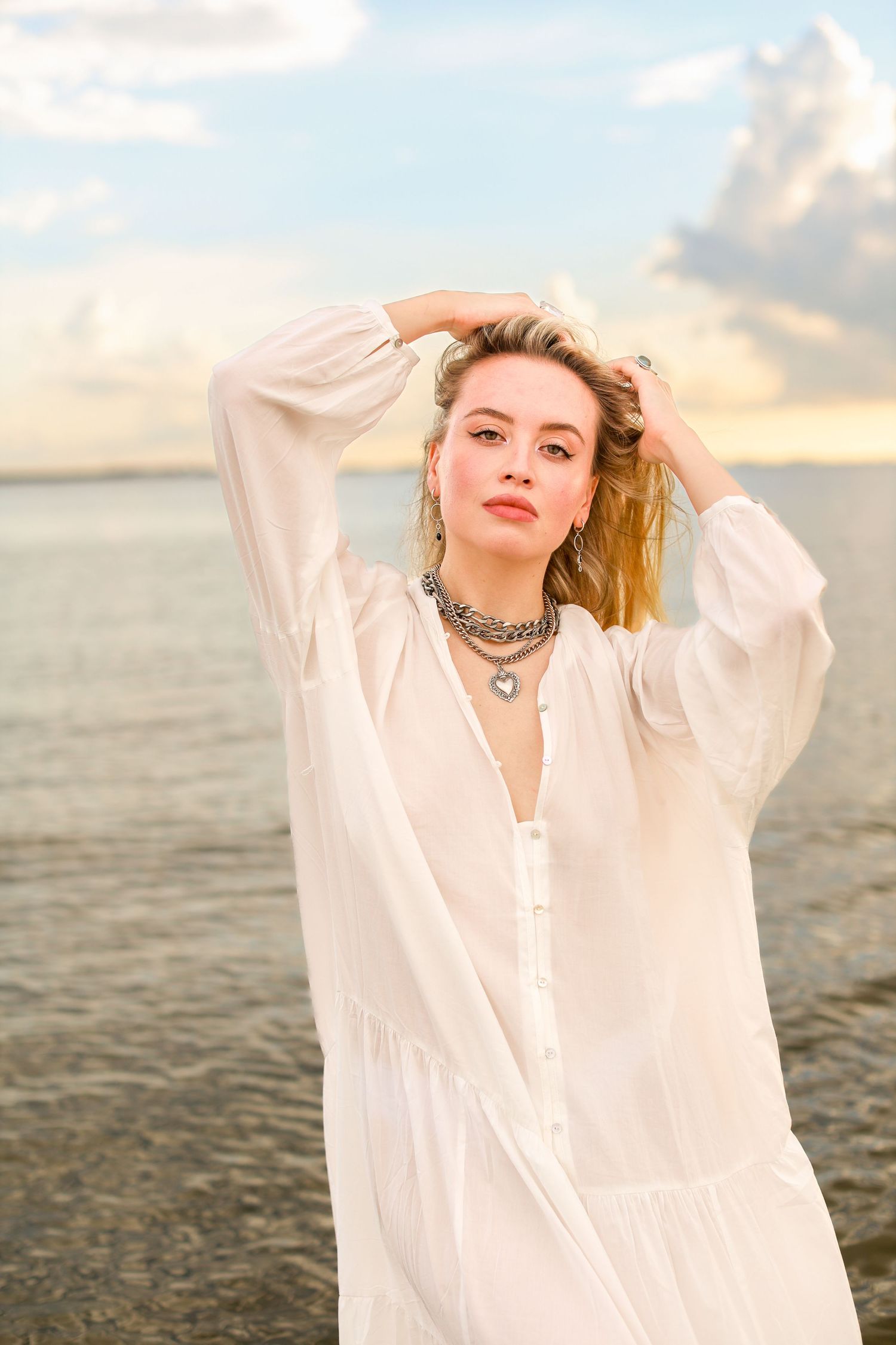 Coastal portrait in flowing white dress and layered necklaces at sunset.