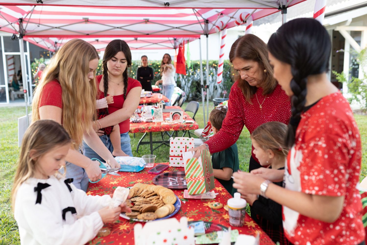 People gathered at tables under red and white striped tent enjoying holiday festivities.