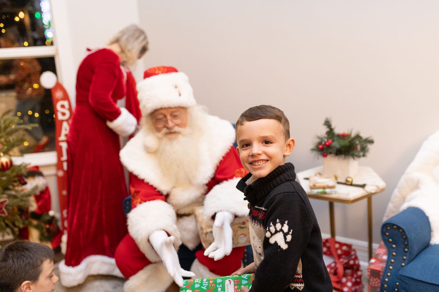 Children gather around Santa Claus during a holiday celebration with a Christmas tree in the background.