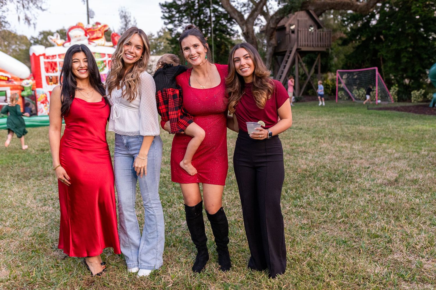 Friends gathered outdoors at a casual event on grassy area with trees in background.