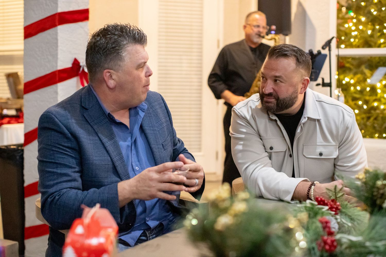 Two men having an animated conversation at a holiday gathering with festive decorations in the background.