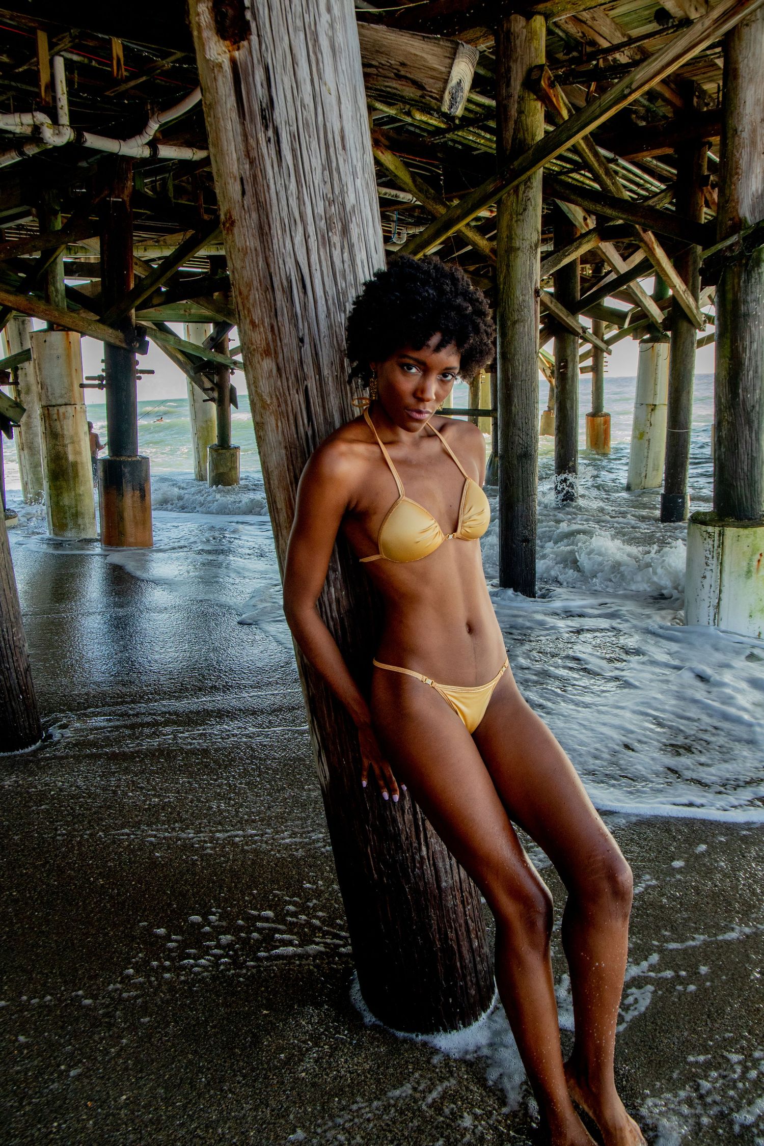 Beachside portrait session underneath wooden pier structure with foamy waves.