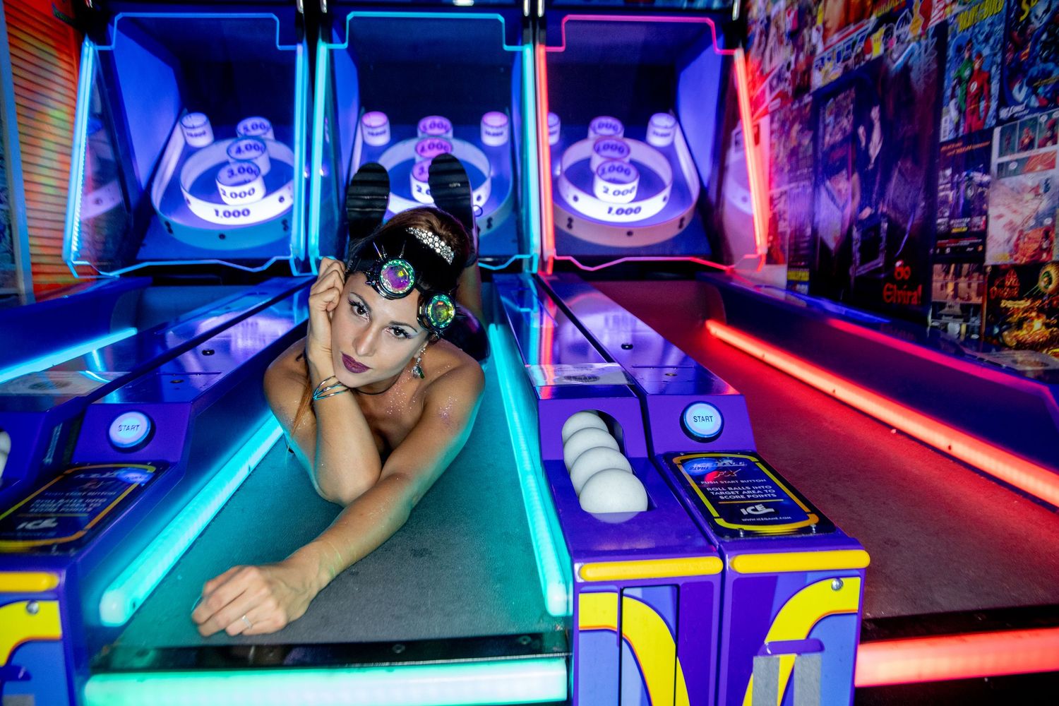Arcade player lying on a skee ball machine surrounded by neon blue lights in a game room.
