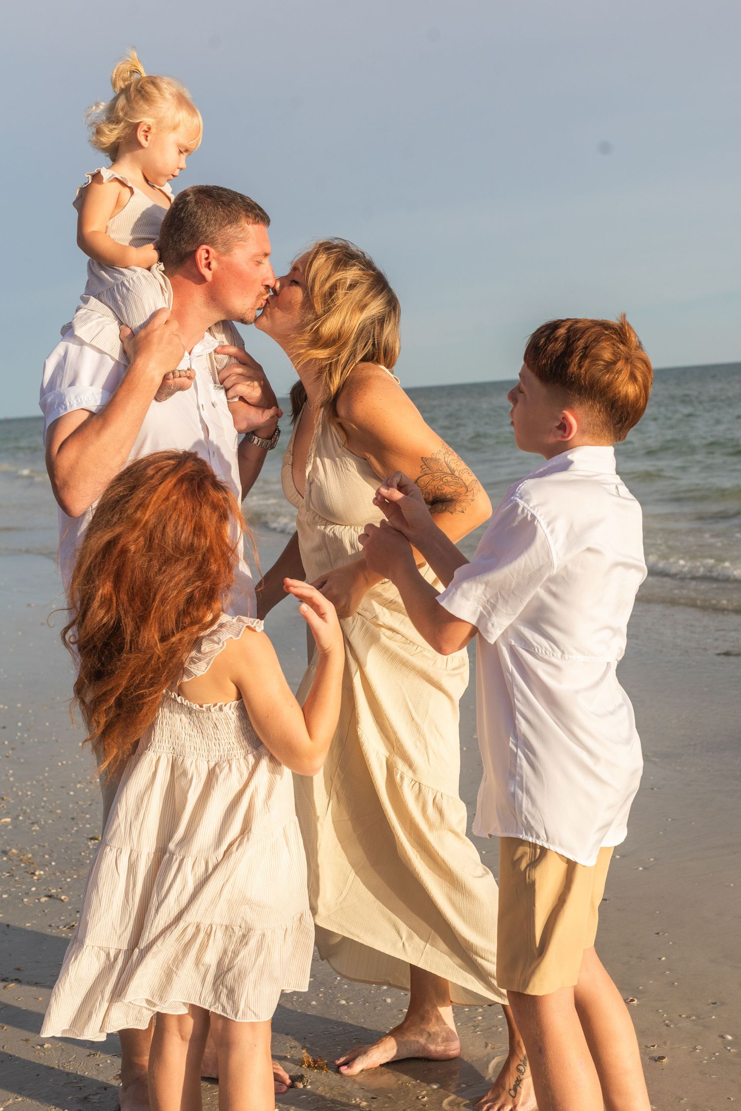 Happy family shares playful moments on the beach at sunset wearing coordinated white outfits.