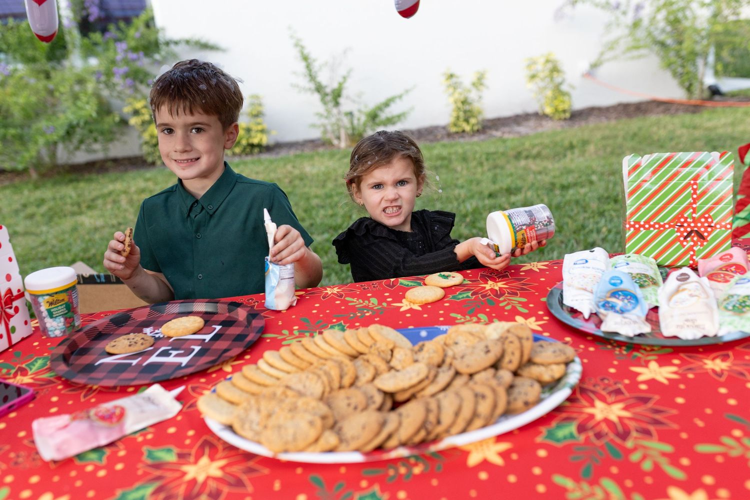 A holiday party table spread with cookies and treats on a red tablecloth with festive decorations.