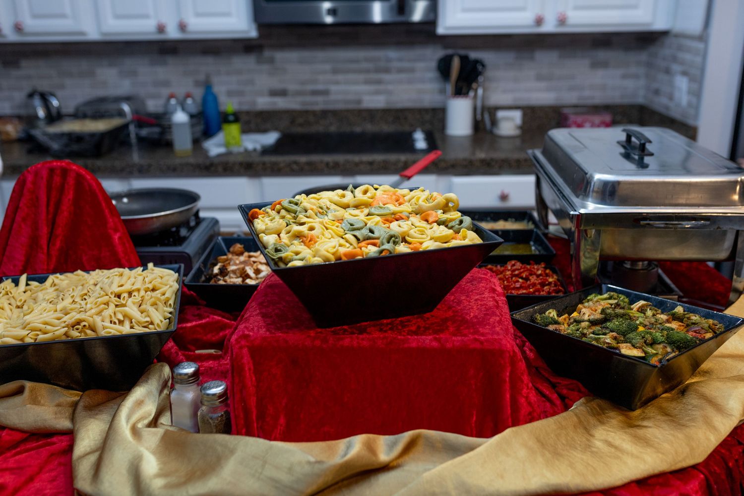 Large trays of food displayed on a red tablecloth at a buffet or catering event.