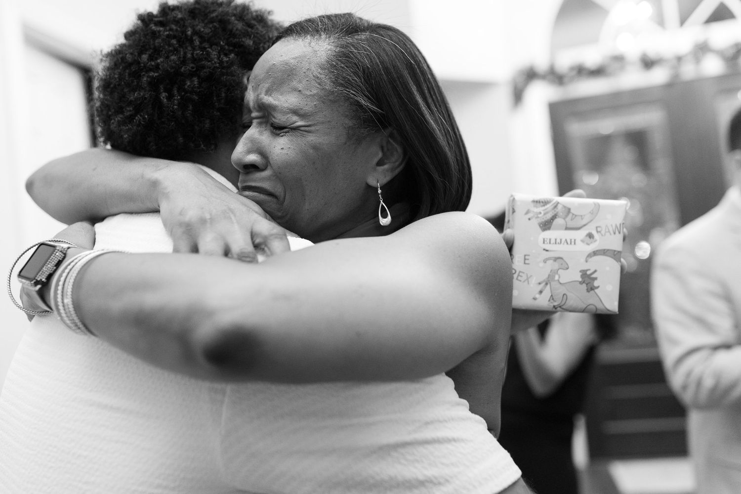 Two people share an emotional embrace while holding a gift in black and white photography.