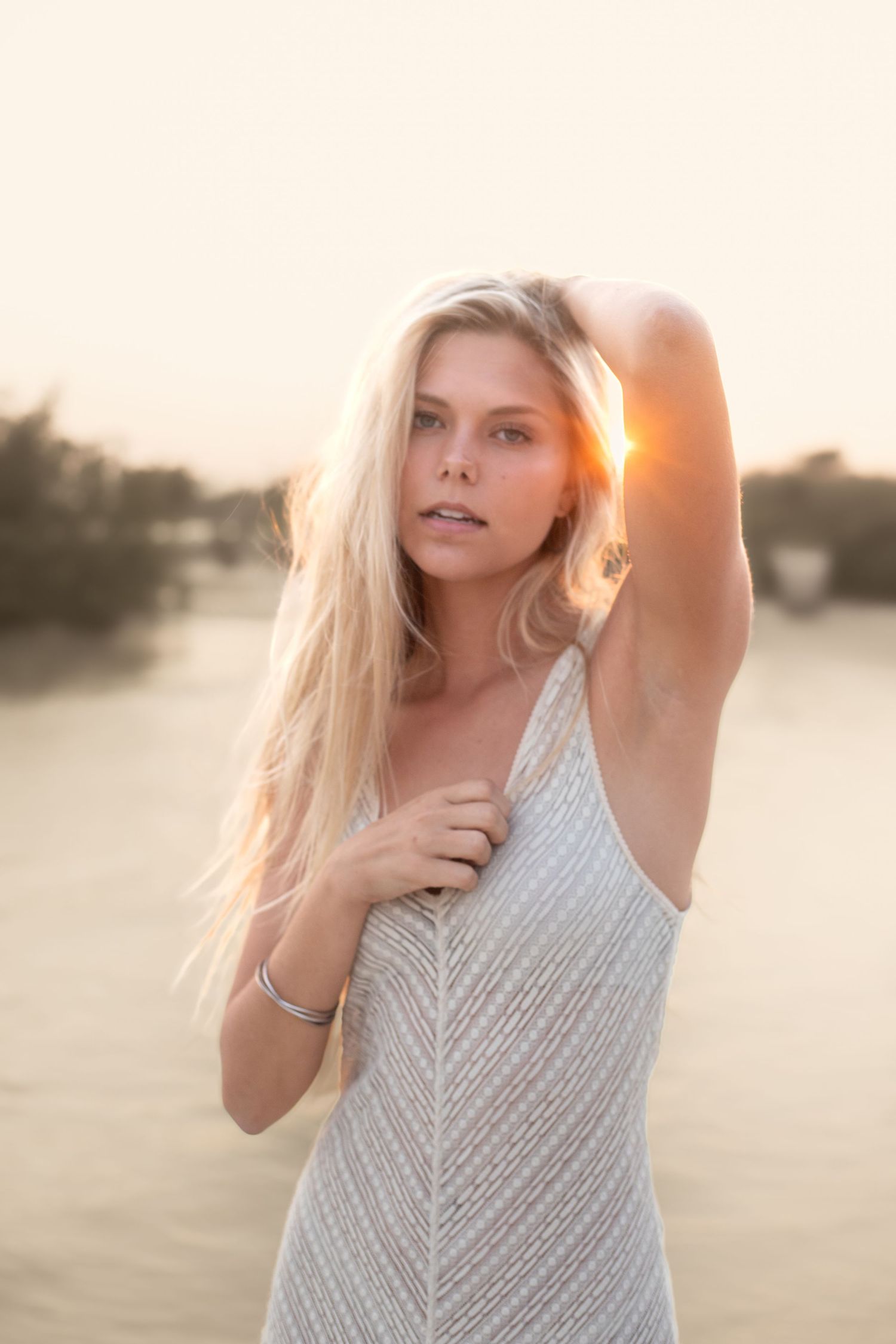 Sunset beach photoshoot in a textured white dress with windswept hair.