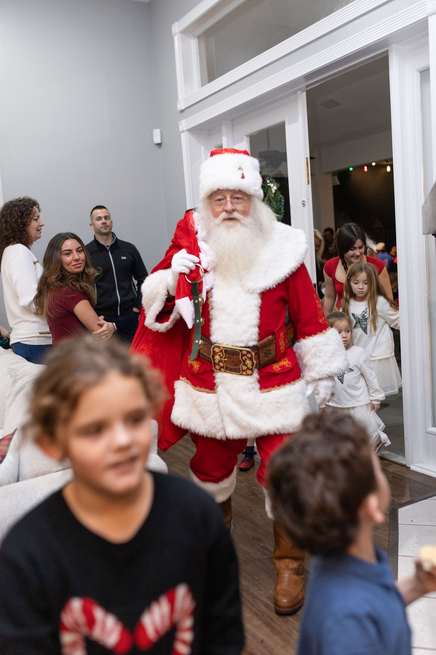 Children and adults celebrate at a holiday party with Santa Claus in a bright indoor space.