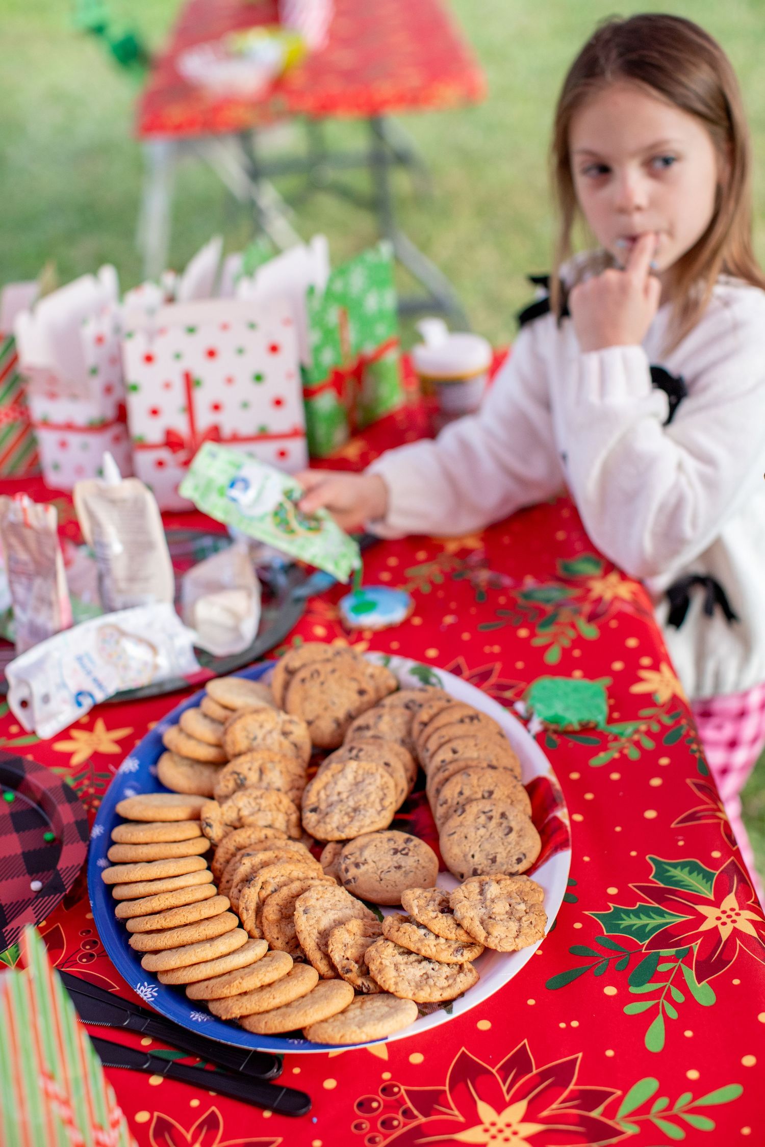 A festive holiday table with plates of freshly baked cookies on a red poinsettia tablecloth.