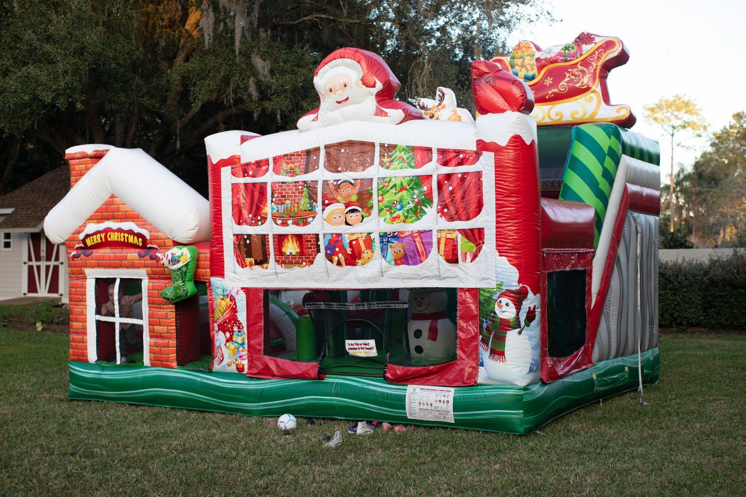Large inflatable holiday decorations set up on grass including Santa's workshop.