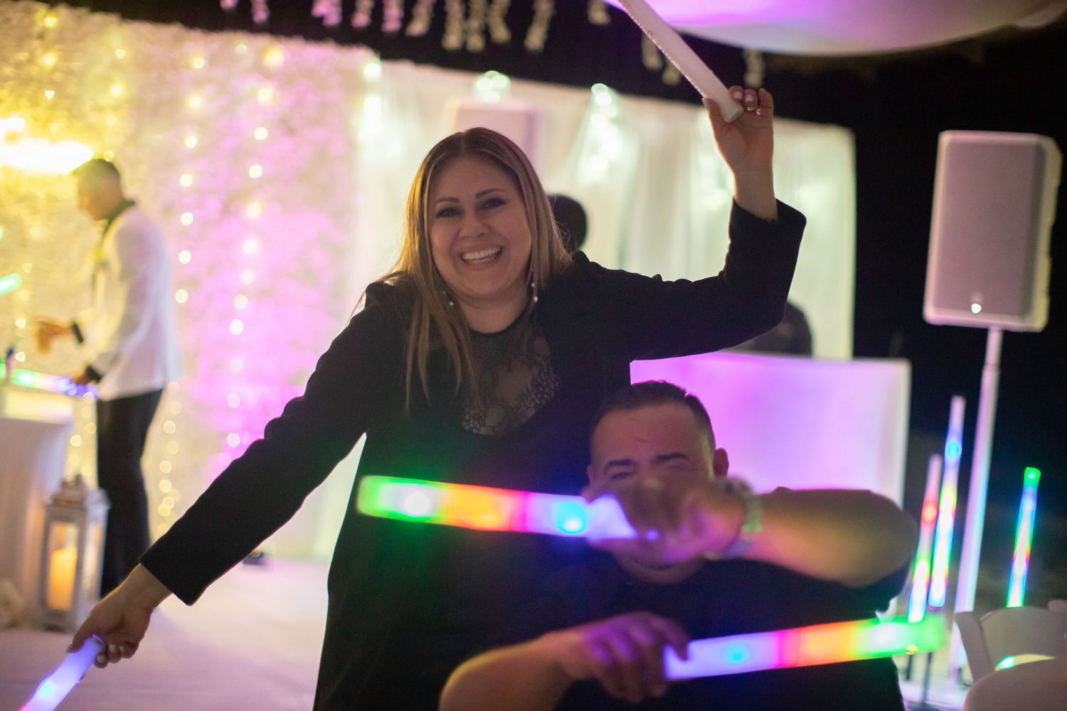 Wedding reception guests dancing and celebrating with colorful LED light sticks on the dance floor.