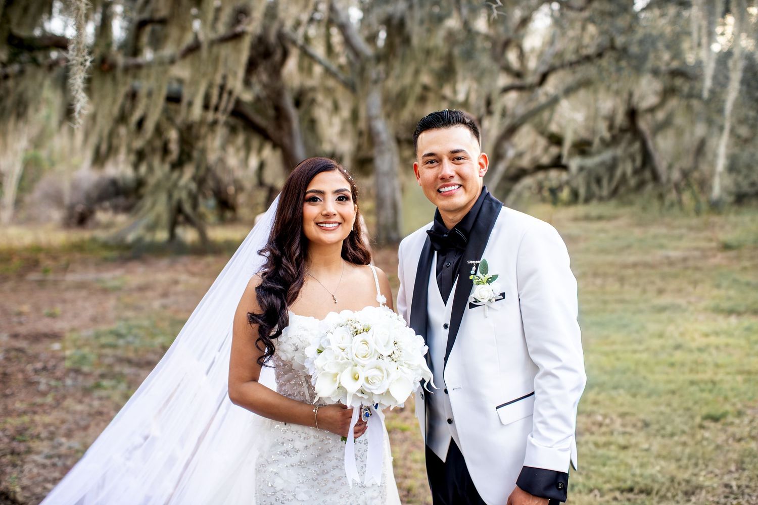 A wedding couple poses together under Spanish moss draped trees in an outdoor setting.