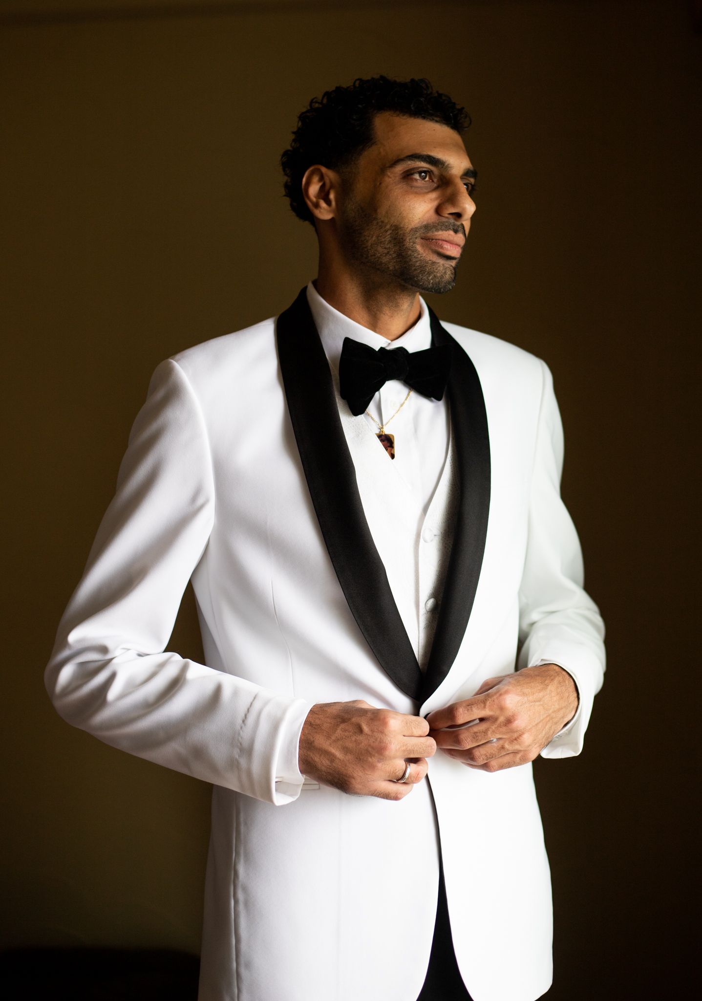 Classic white tuxedo with black lapels being adjusted in dramatic lighting.