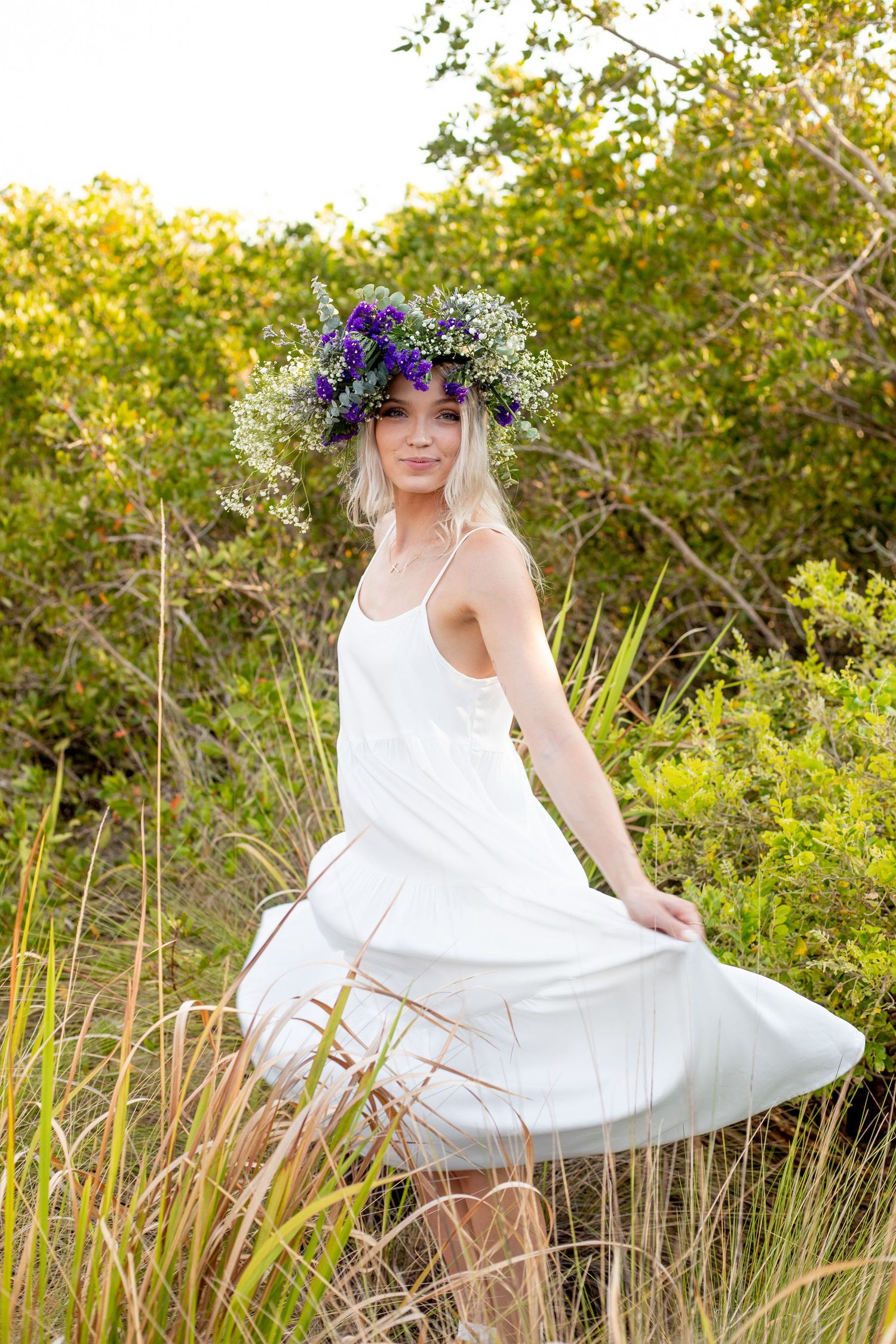 White sundress twirling photoshoot among tall grass and greenery at sunset.