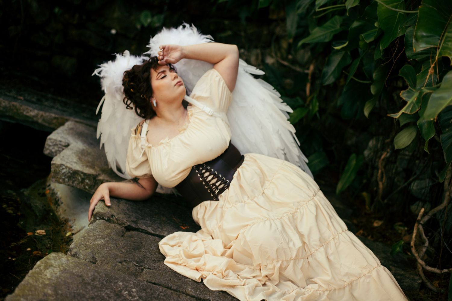 Moody garden photography with flowing cream dress and angel wing accessories.
