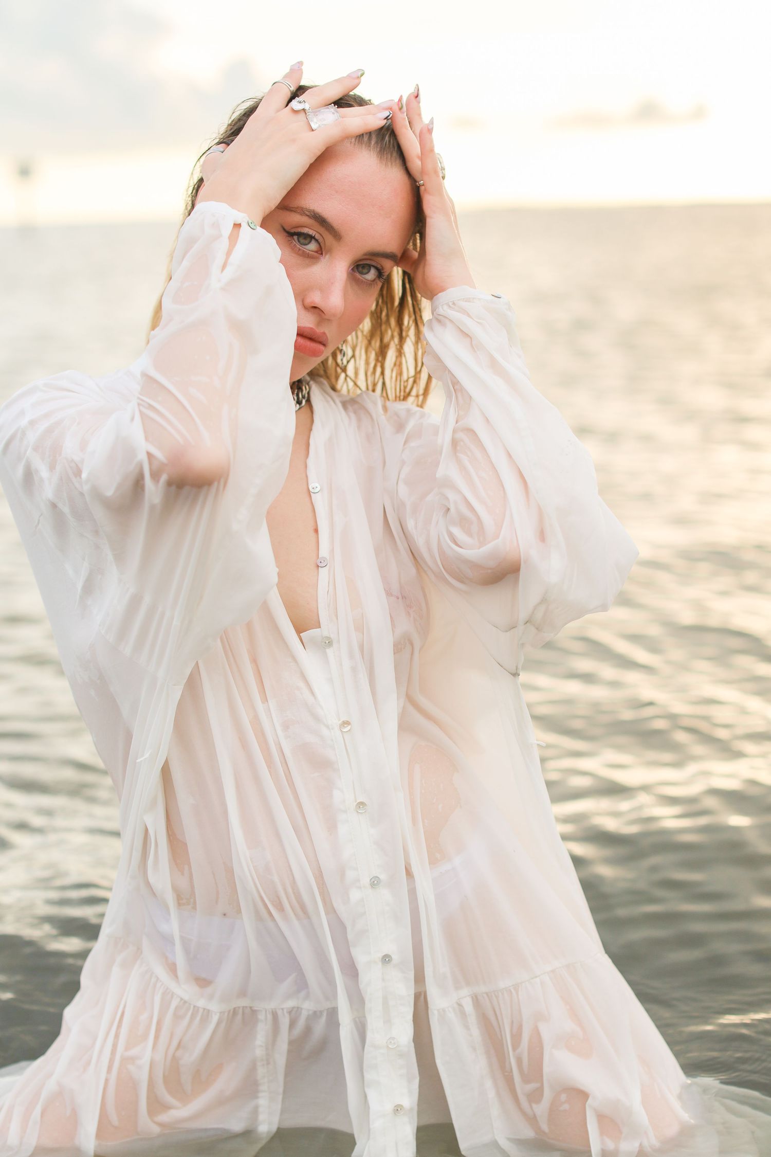 Ethereal photoshoot in a white sheer dress by the water during golden hour.