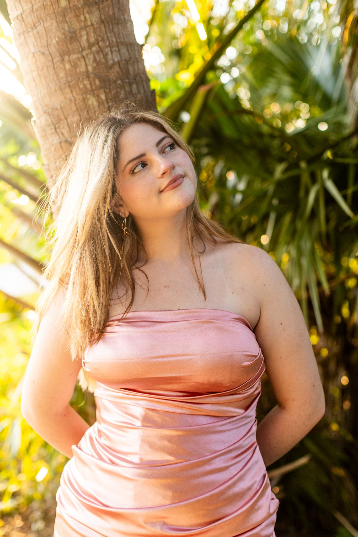 Soft pink dress glowing in tropical garden setting with palm trees.