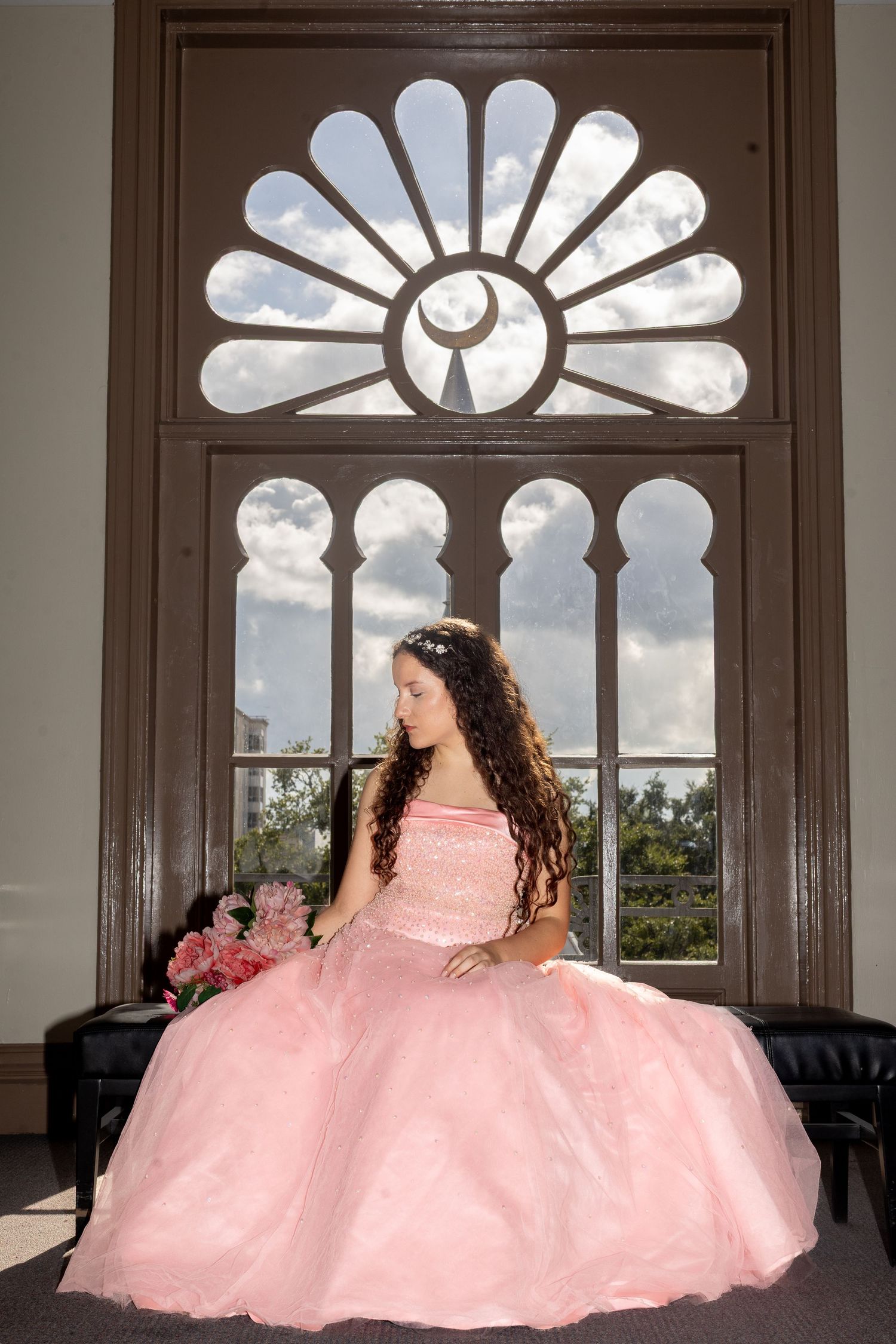 Pink ballgown photographed against decorative fan window with dramatic lighting.