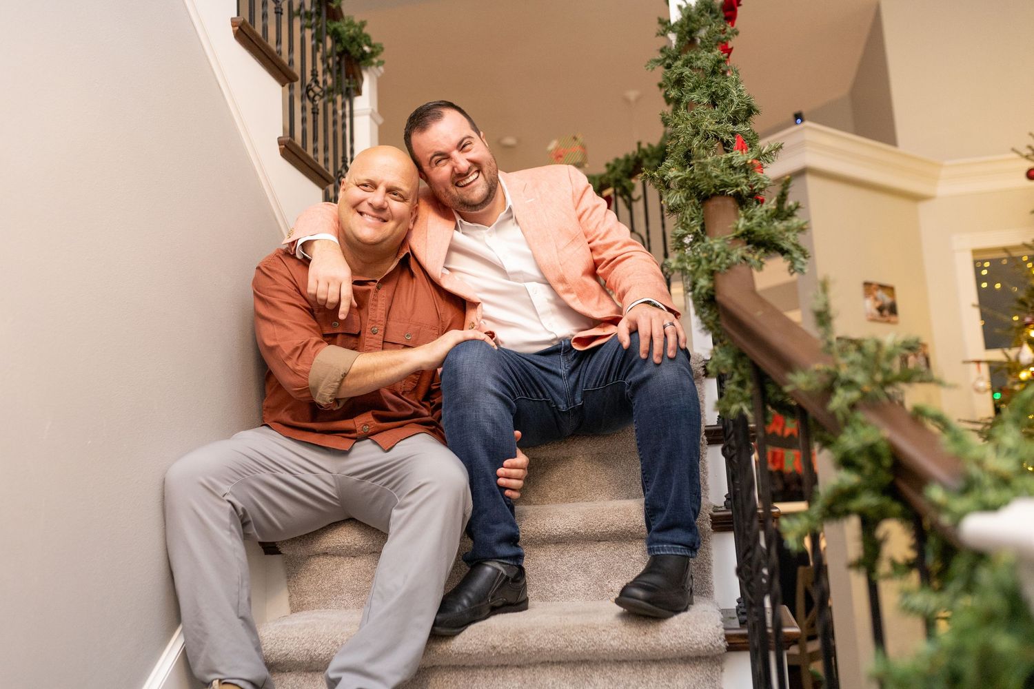 People in formal attire gathered on carpeted stairs decorated with holiday greenery for a group photo.