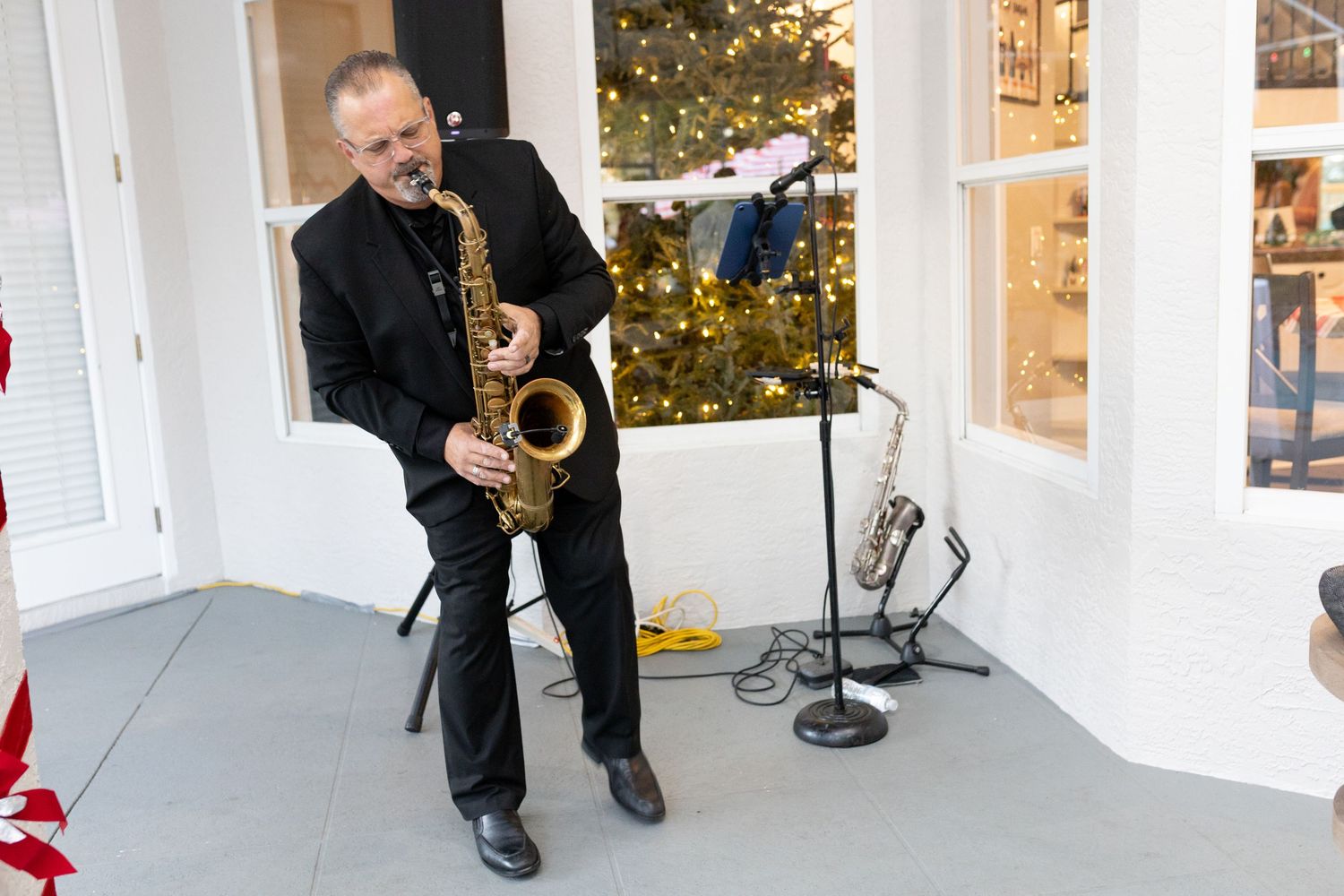 Saxophonist performing in front of white columns and holiday decorations.