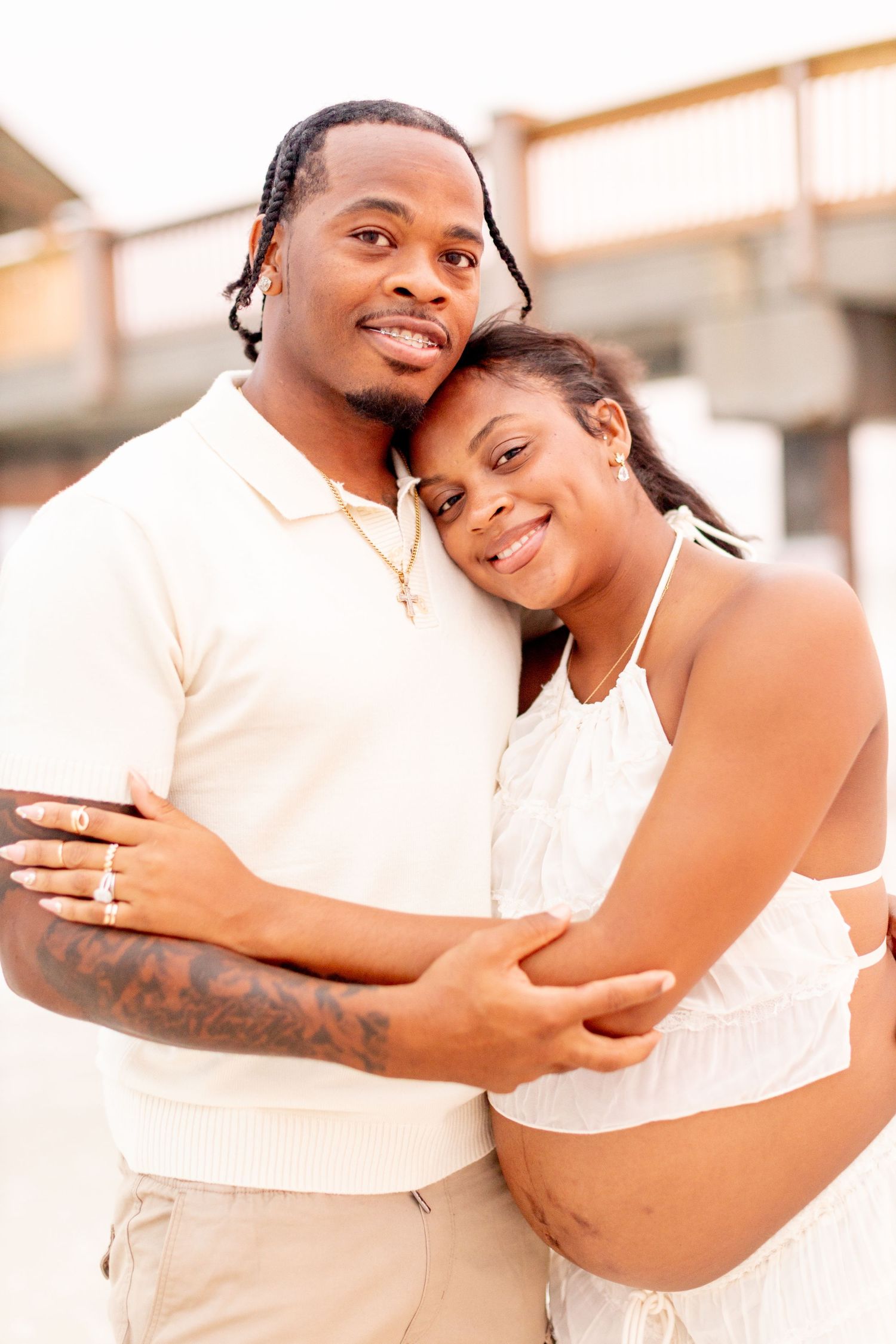 A couple embraces on the beach while wearing coordinated white and cream colored outfits.