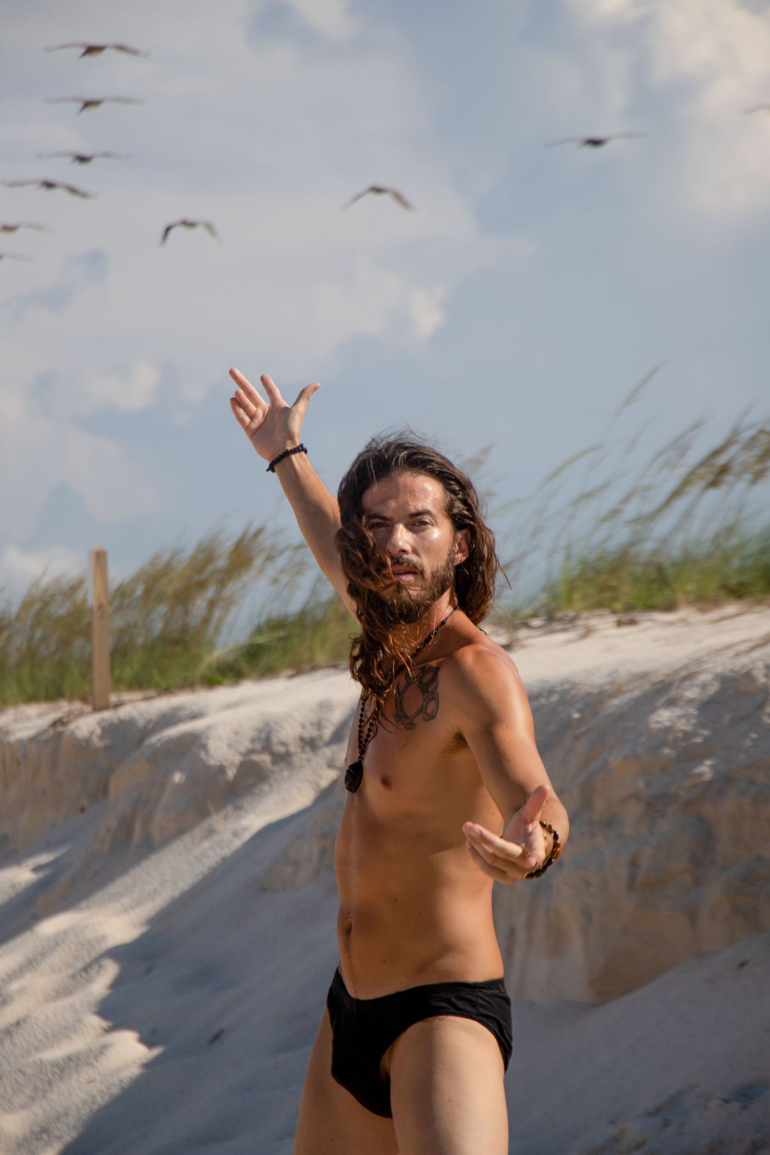 Silhouette poses on beach with arms outstretched as seabirds fly overhead.