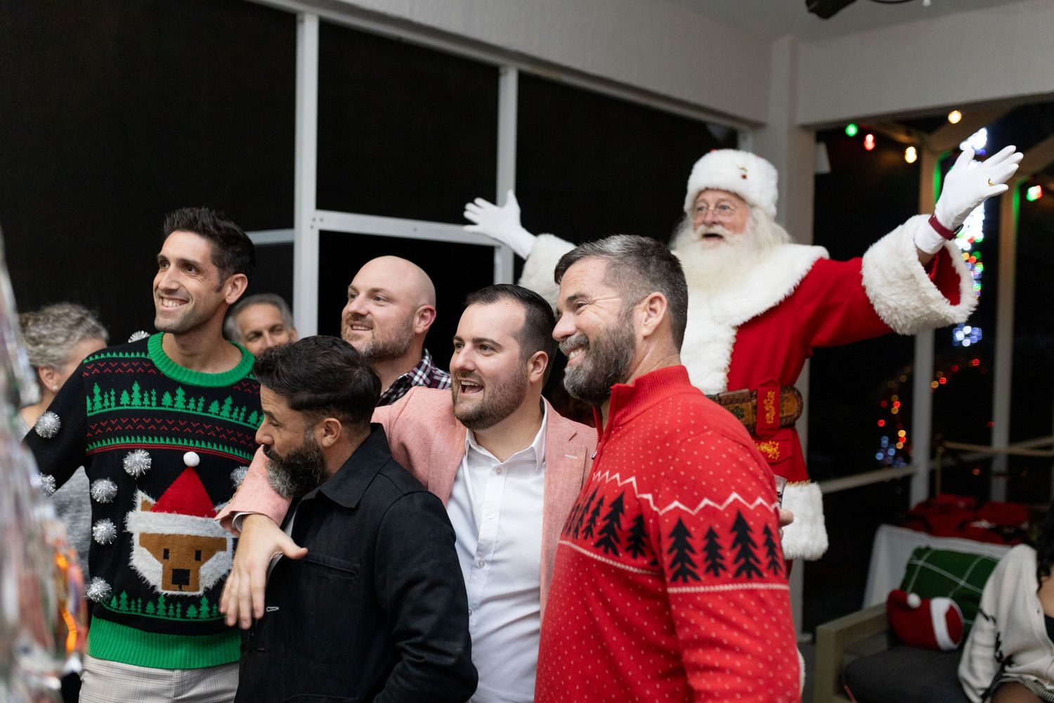 Festive group photo with Santa and partygoers in holiday sweaters.
