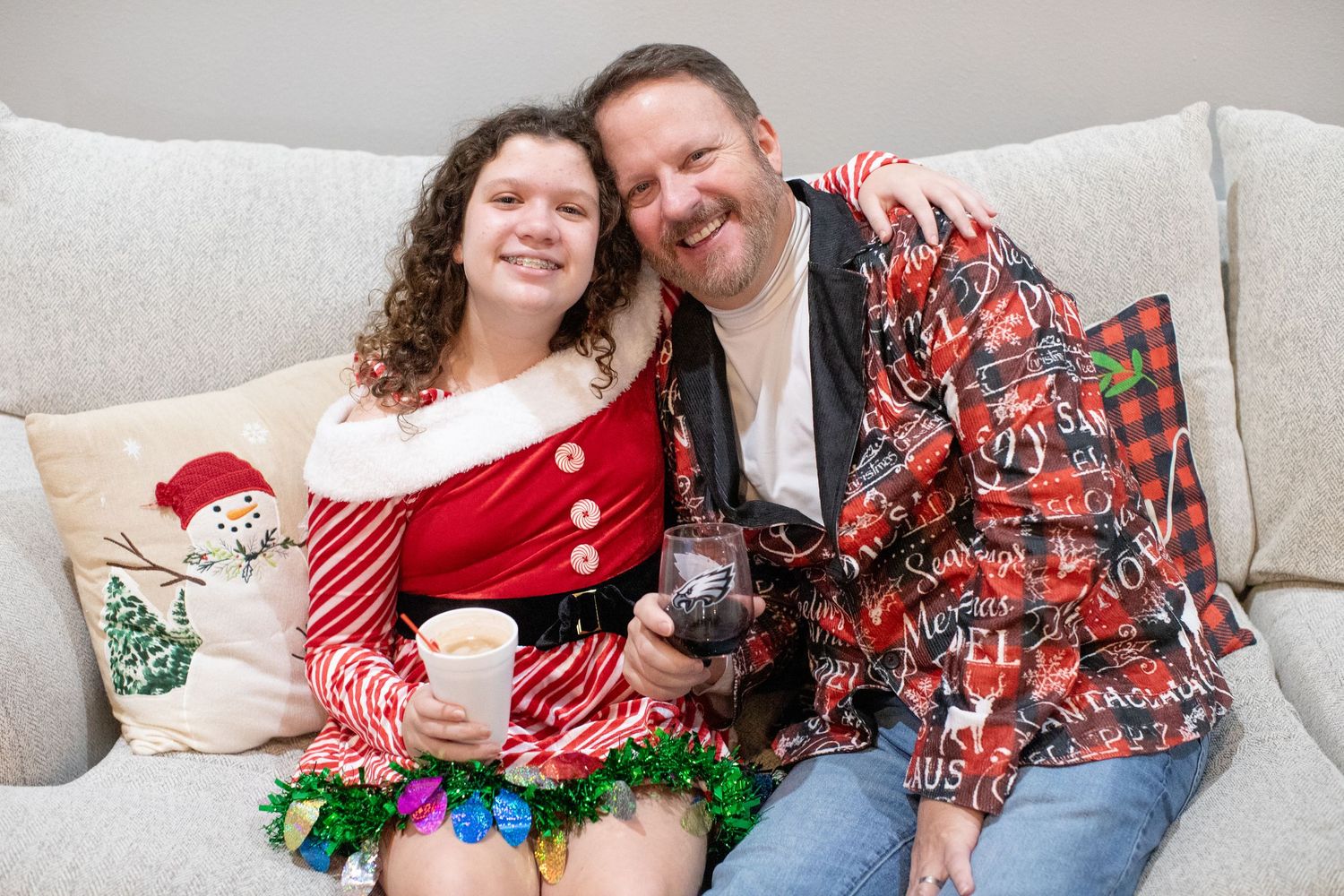 Family wearing festive holiday attire poses together on light colored couch.